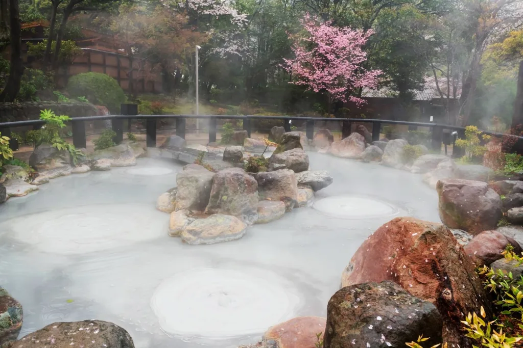 Oniishibozu Jigoku thermal baths surrounded by cherry blossom trees in Beppu Japan